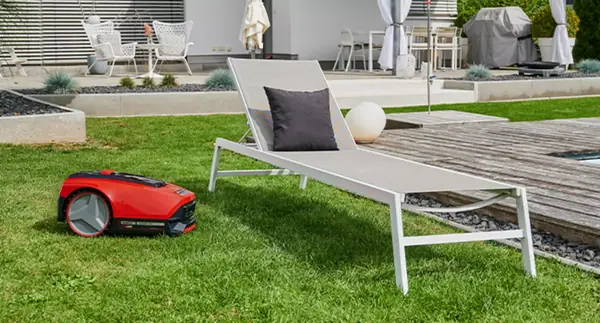 Robotická sekačka Einhell FREELEXO SMART 750 se pohybuje po trávníku, v pozadí je zahradní salonek.