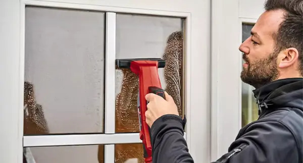 Muž čistí malé okno aku čističem oken Einhell BRILLIANTO s úzkou hubicí ze sady trysek