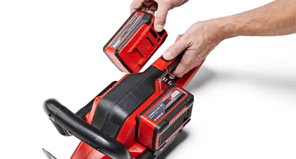 Akumulátor Einhell Power X-Change je vkládán do zahradního nářadí se dvěma přihrádkami pro akumulátory, na bílém pozadí